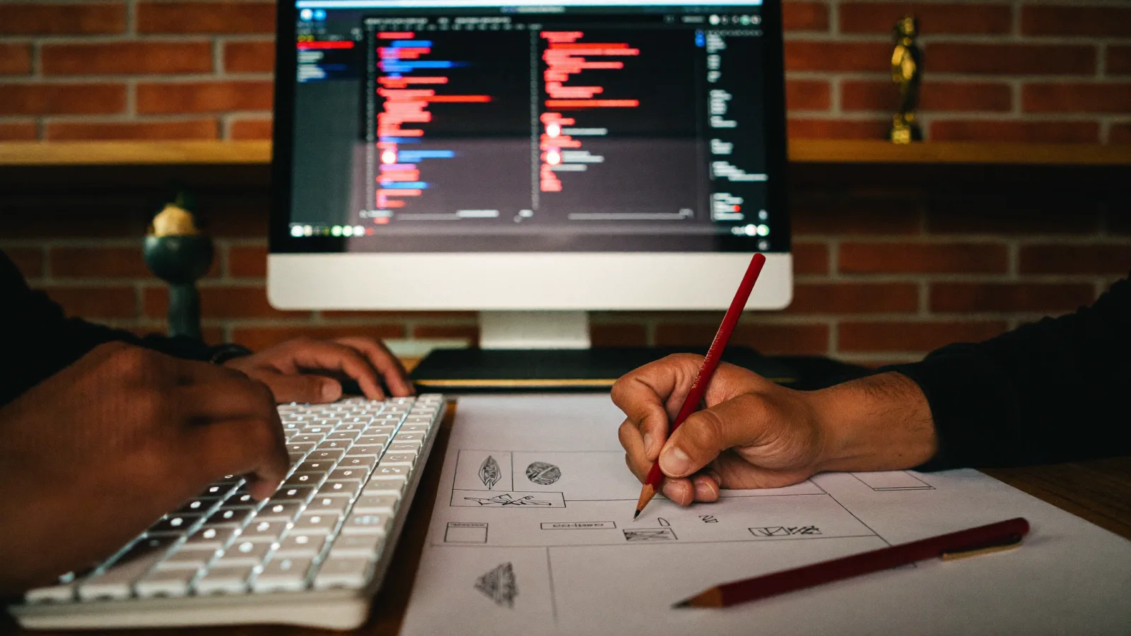 Designer sketching wireframes beside a screen of code